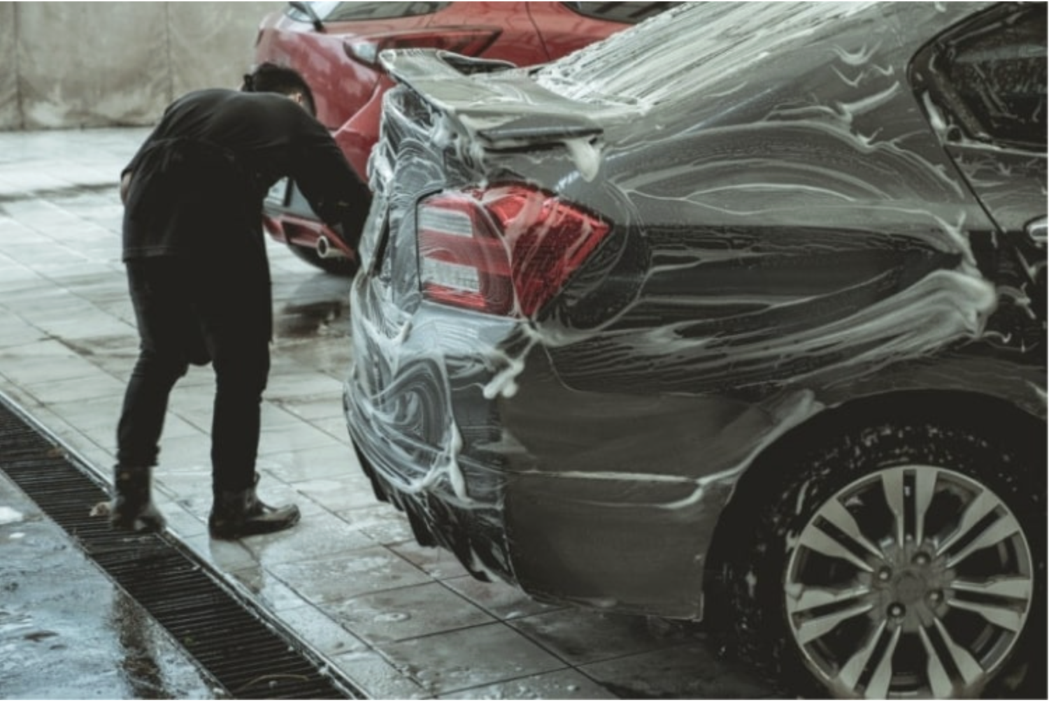 Detailer foam-washing a black sedan exterior